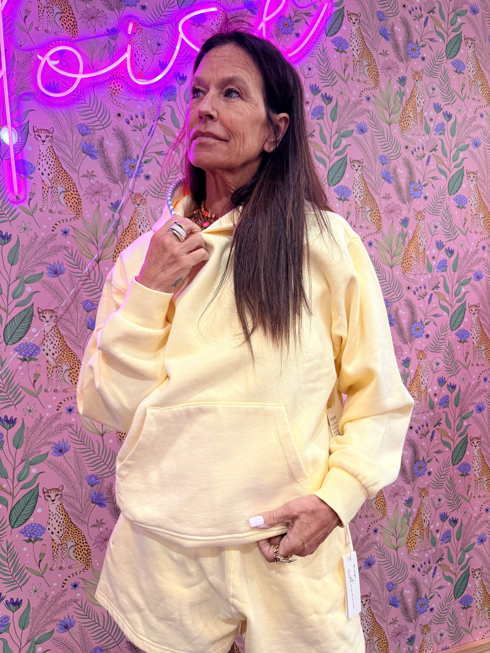 Woman wearing light yellow hoodie on pink floral background