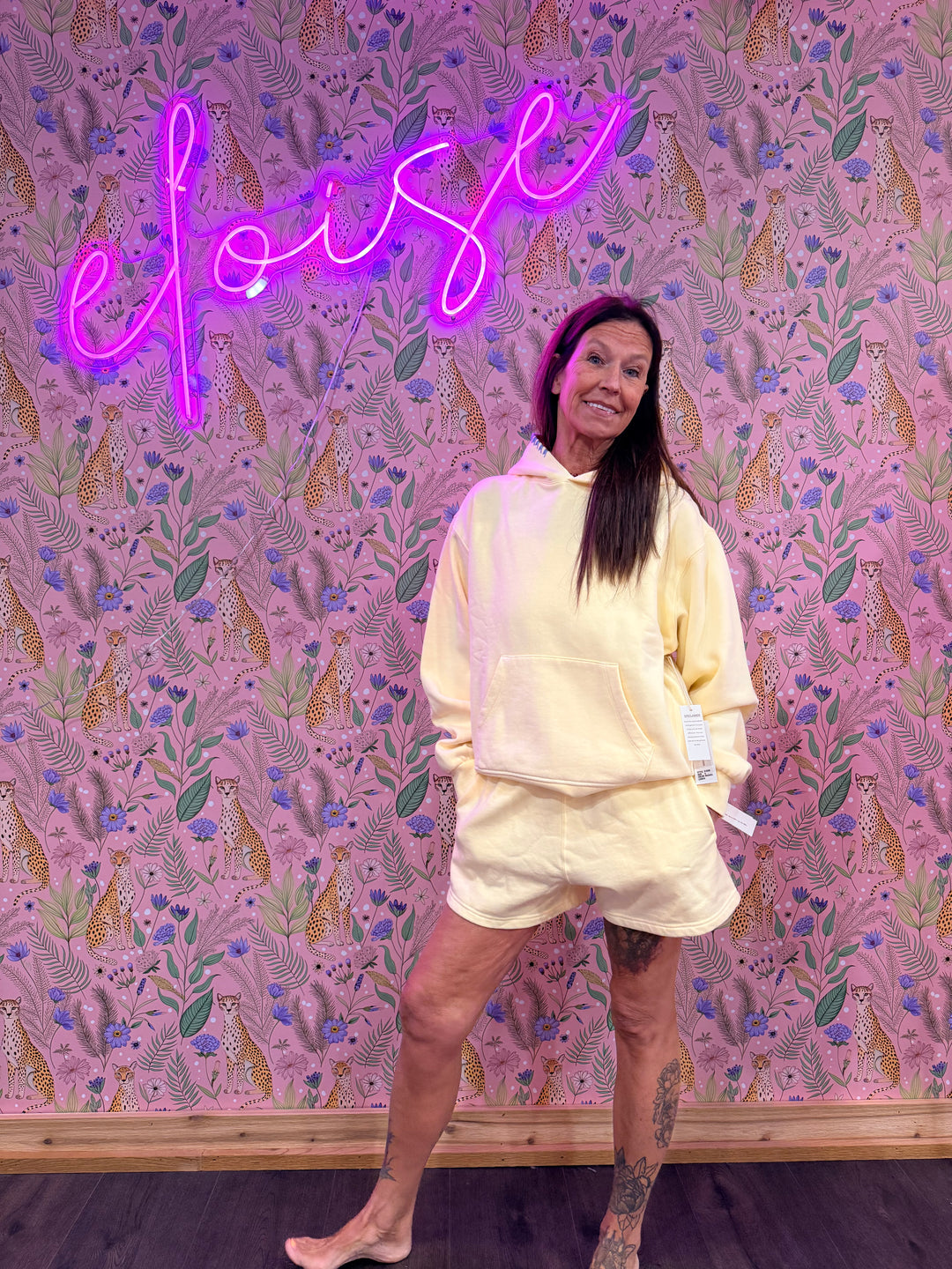 Woman wearing matching light yellow hoodie and sweat shorts on pink floral background