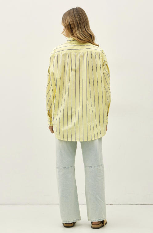 Woman shown from behind wearing yellow stripe button up and jeans on plain background