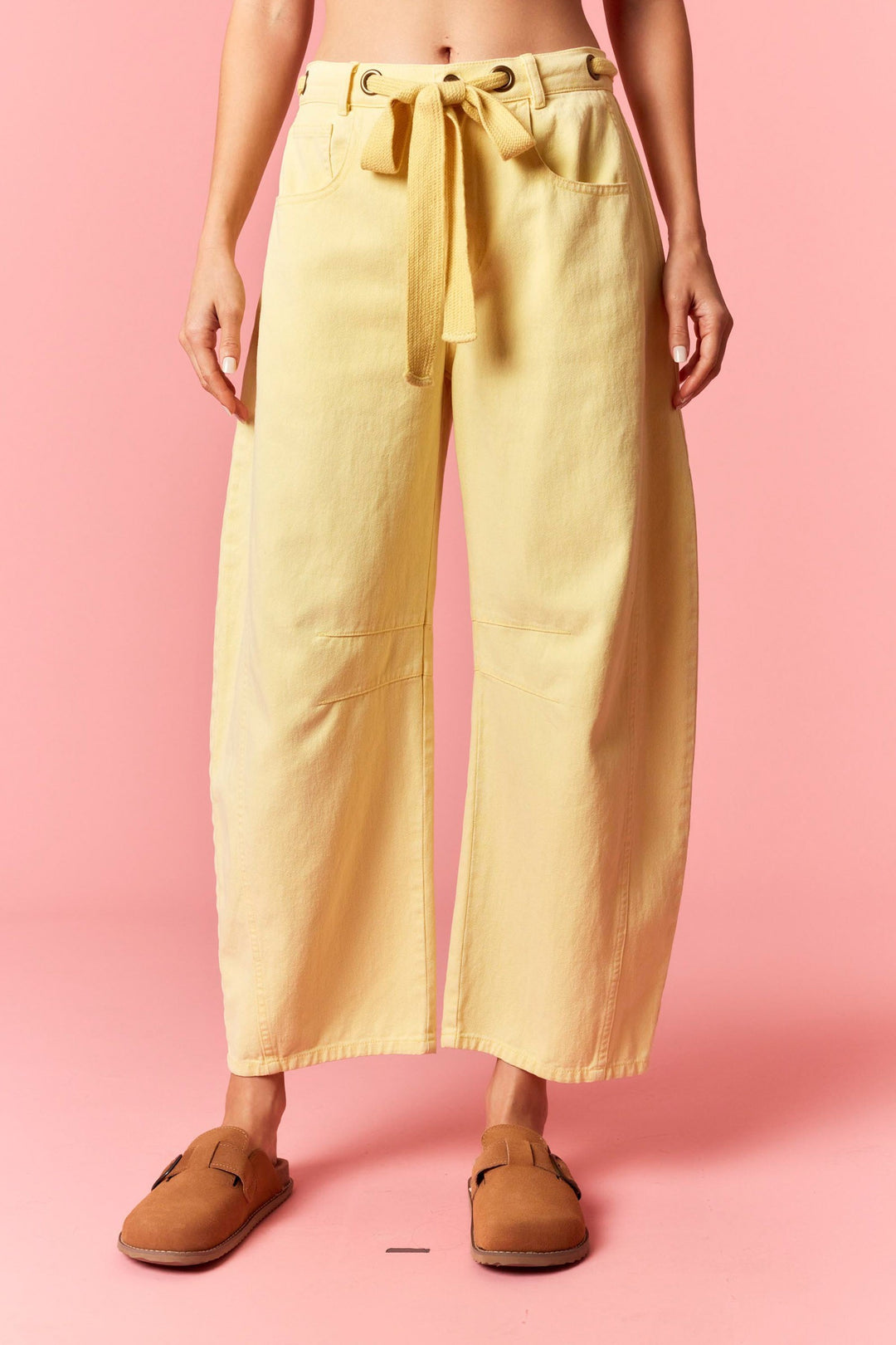 Person wearing yellow wide-leg pants and brown shoes on a pink background