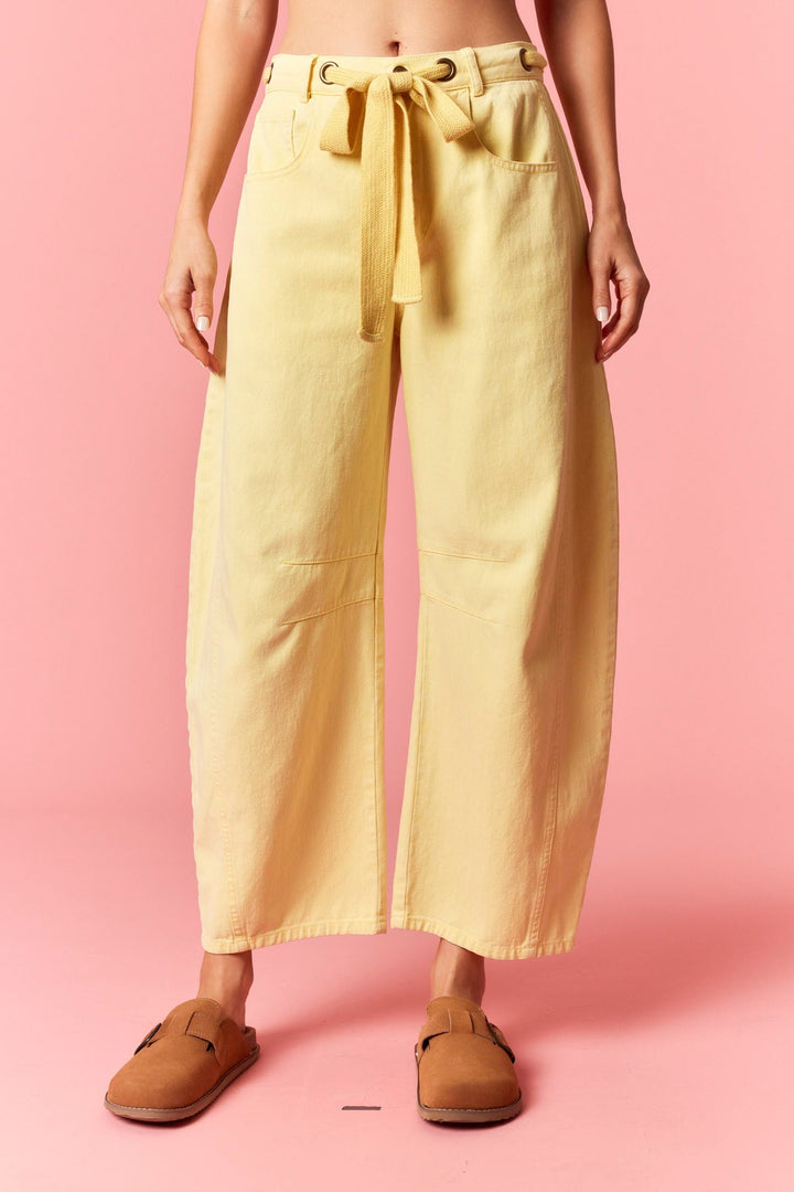 Person wearing yellow wide-leg pants and brown shoes on a pink background