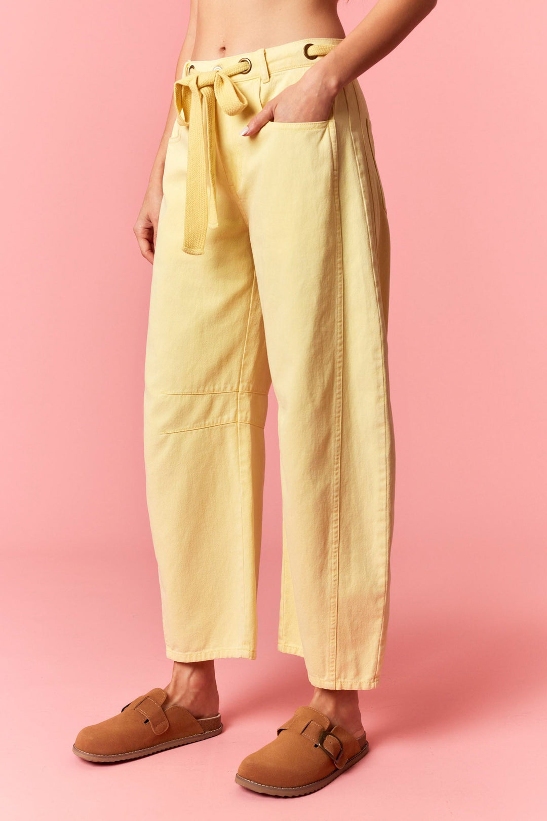 Person wearing yellow pants with a belt on a pink background
