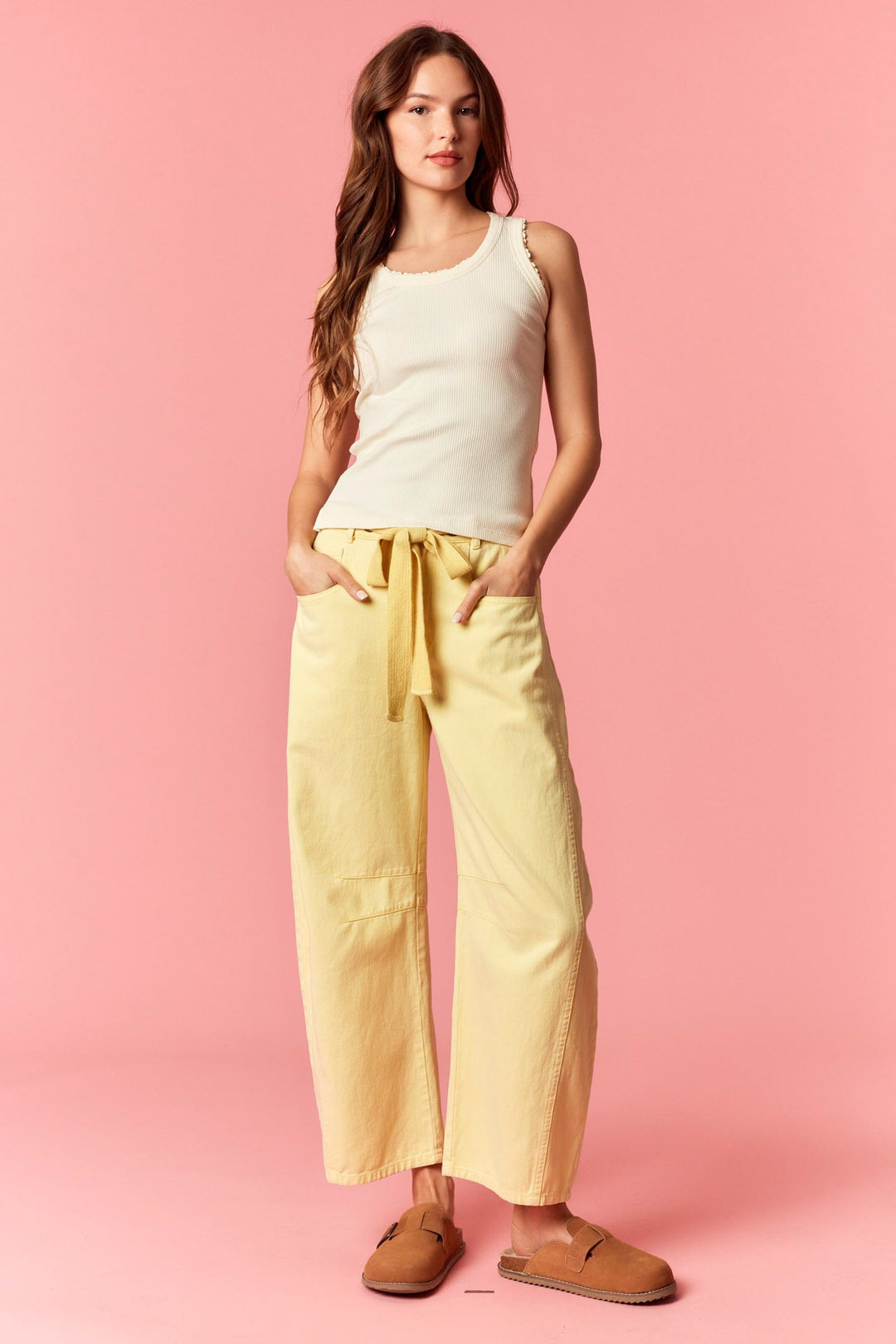 Woman wearing a white tank top and yellow pants against a pink background
