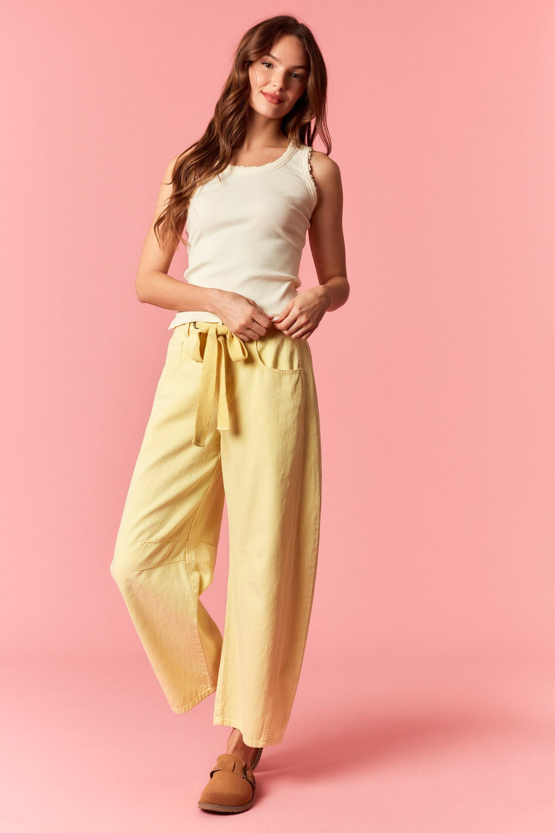 Woman wearing a white sleeveless top and yellow pants on a pink background