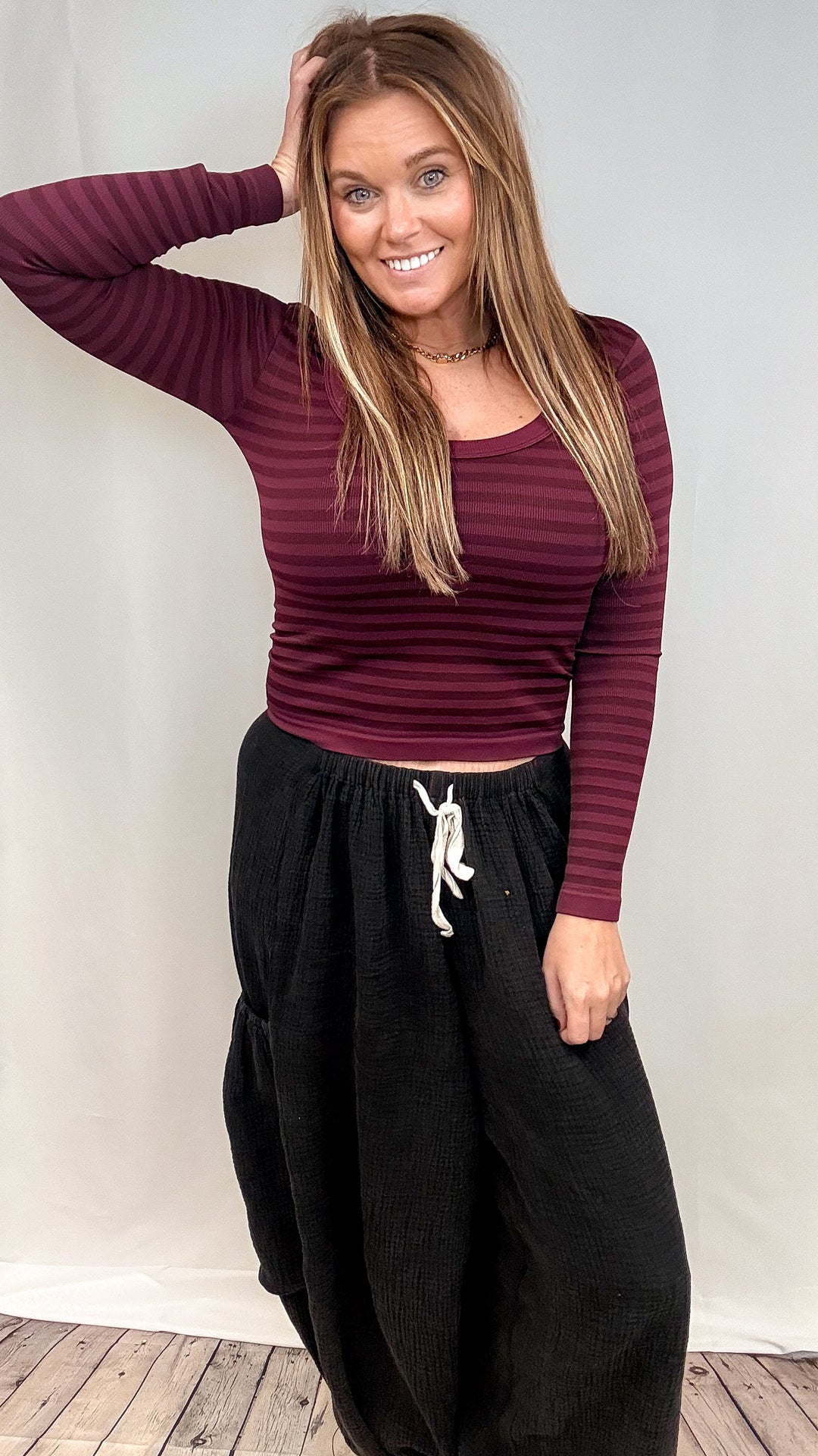 Woman wearing burgundy stripe long sleeve top and black pants on plain background