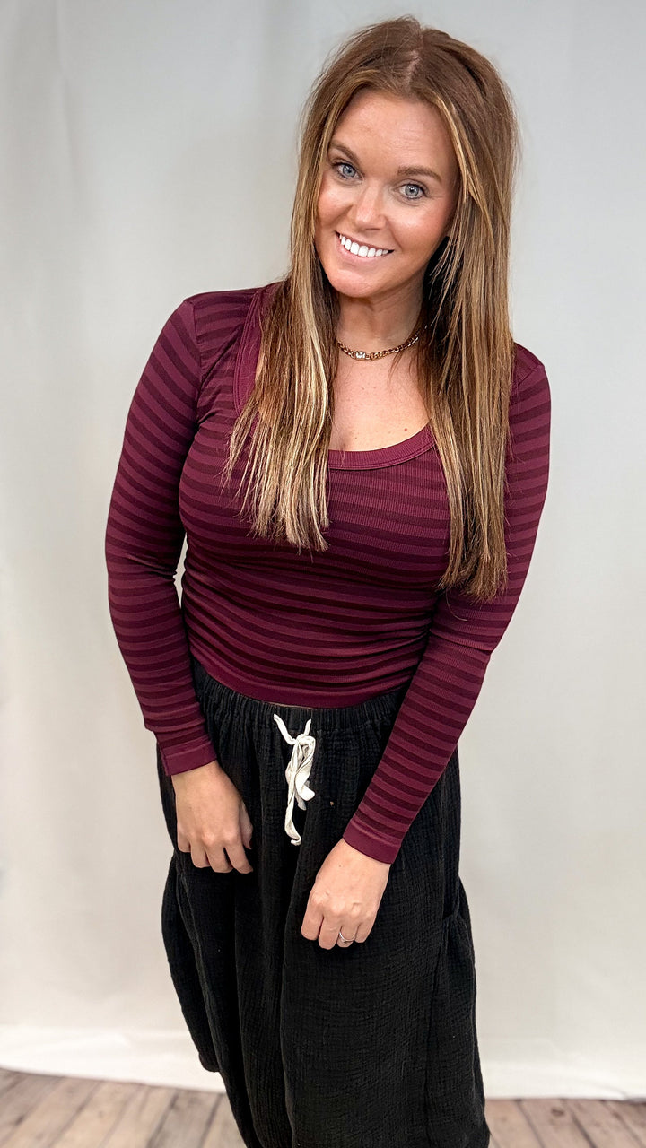 Woman wearing burgundy stripe long sleeve top and black pants on plain background