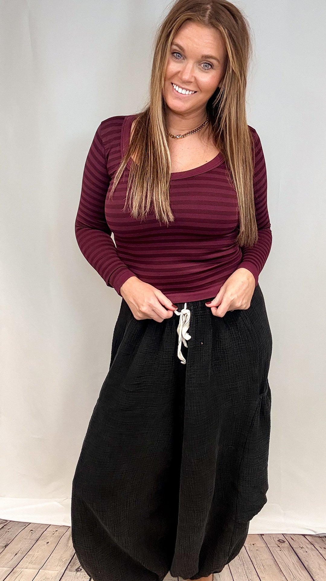 Woman wearing burgundy stripe long sleeve top and black pants on white background