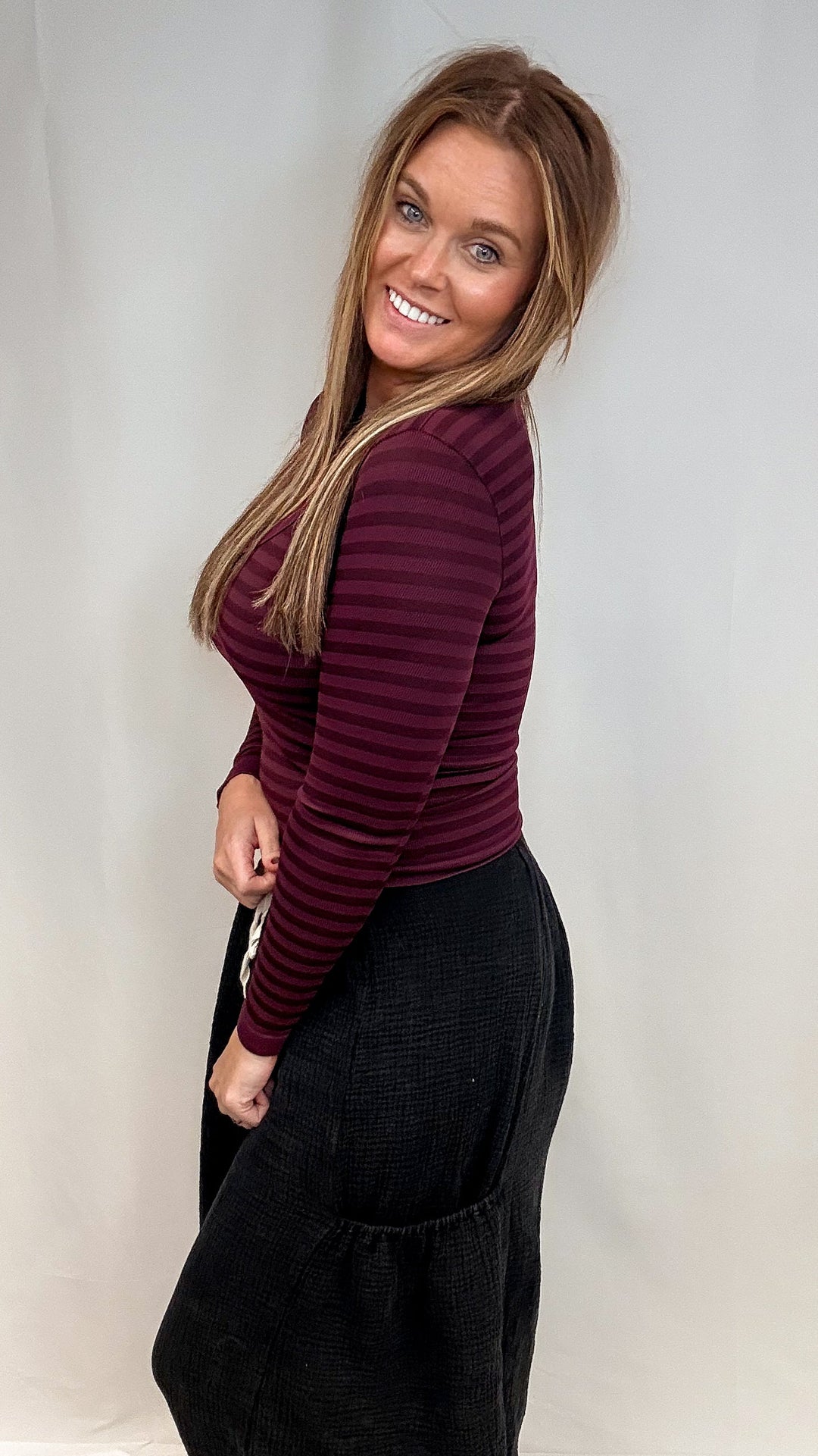 Woman wearing burgundy stripe long sleeve top and black pants on white background