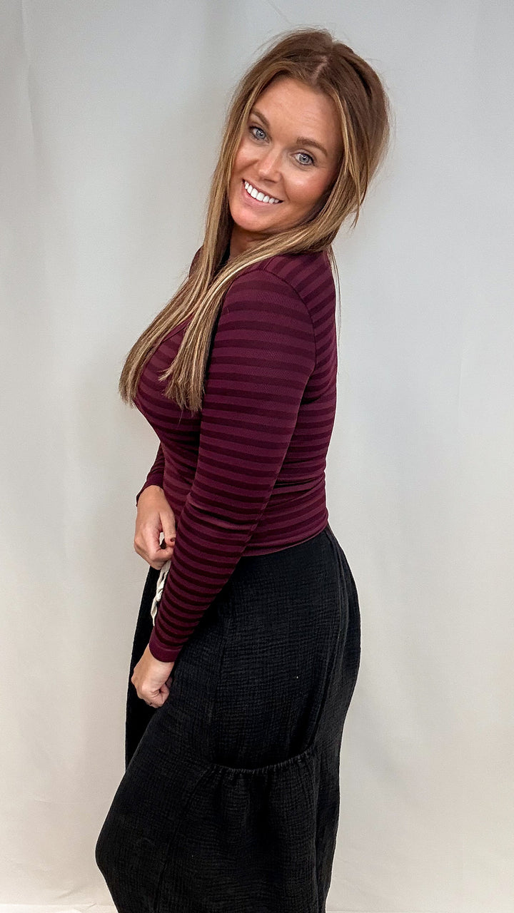 Woman wearing burgundy stripe long sleeve top and black pants on white background
