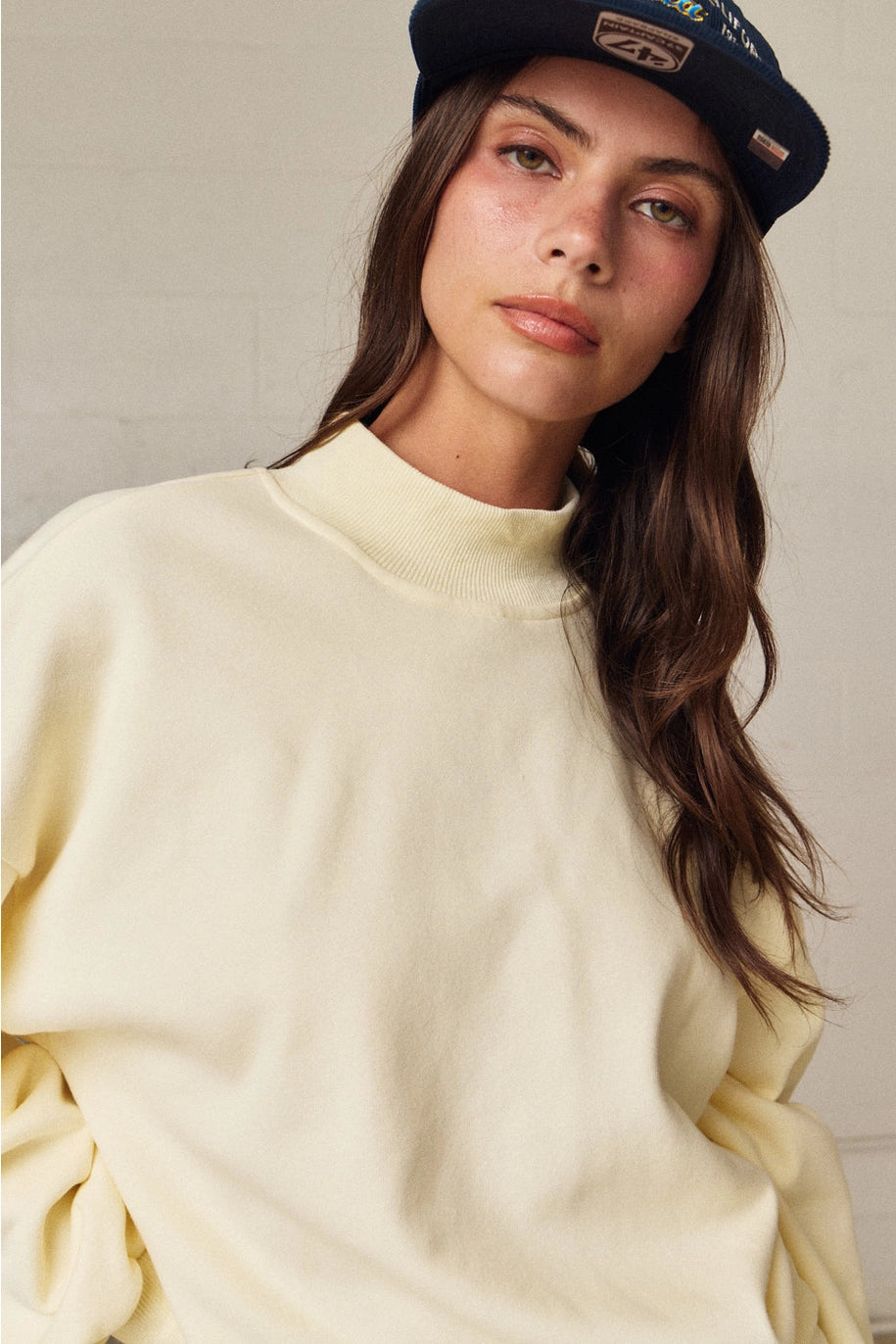 Woman wearing a light yellow sweater and navy cap against a neutral background
