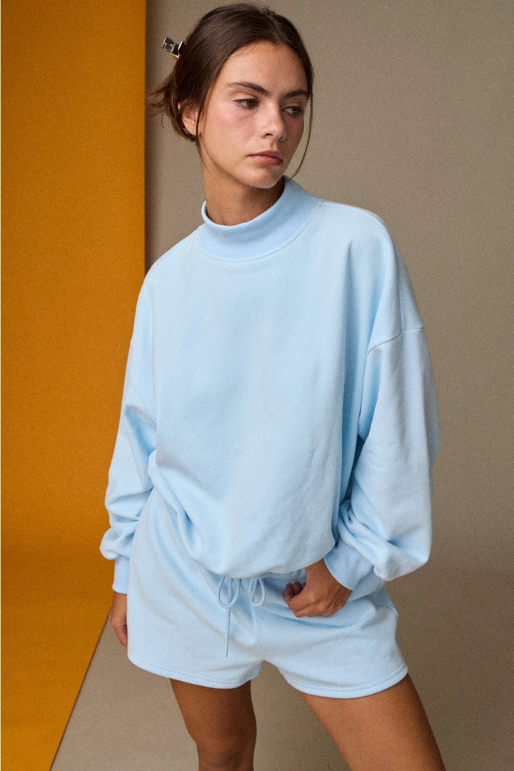 Woman wearing a light blue outfit against a gradient wall.