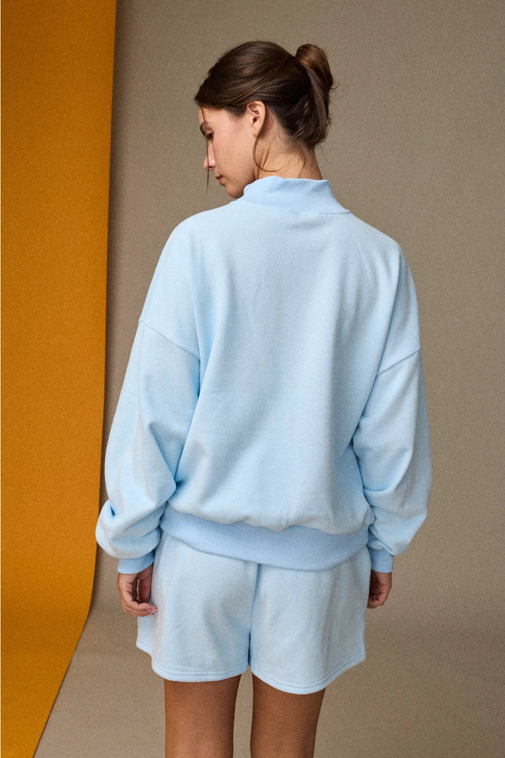 Person wearing a light blue tracksuit against a beige wall.