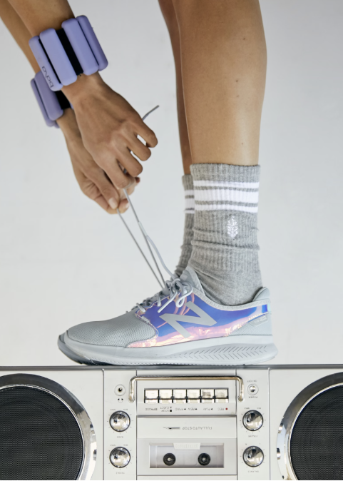 Person wearing grey stripe tube socks with tennis shoes standing on boombox on plain background