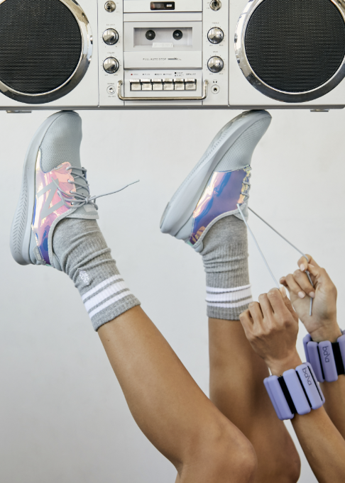 Person wearing grey stripe tube socks with tennis shoes holding up boombox on plain background
