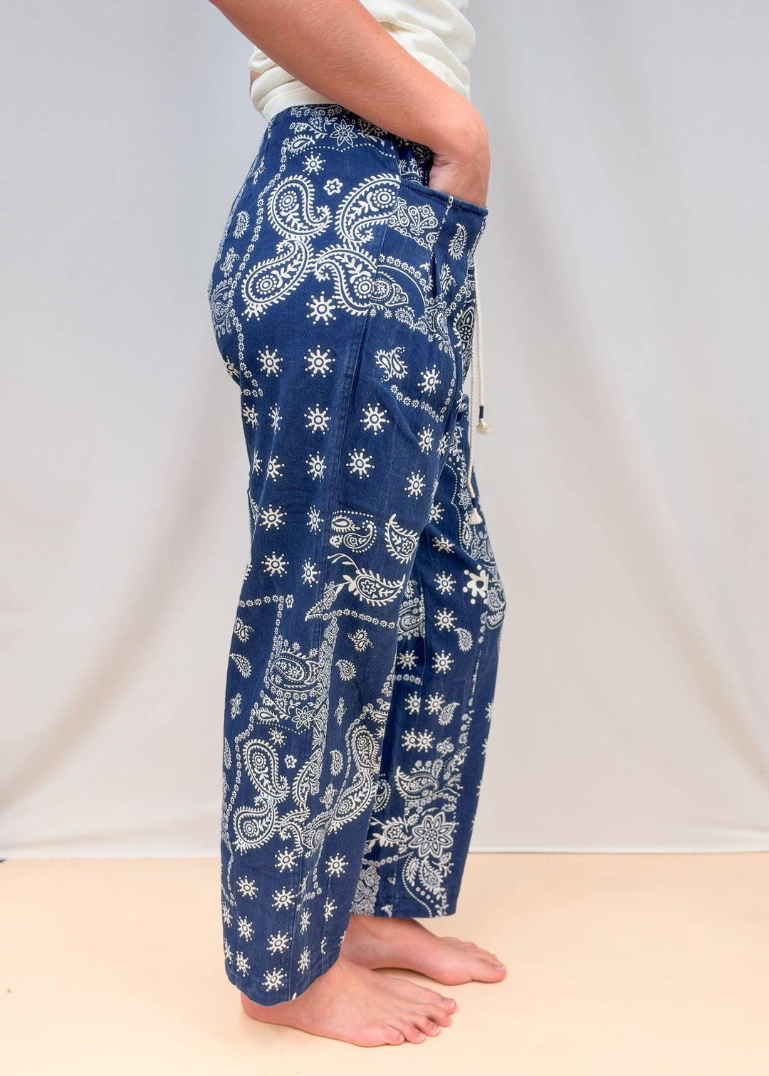 Woman shown from side view waist down wearing blue paisley pull on pants on plain background