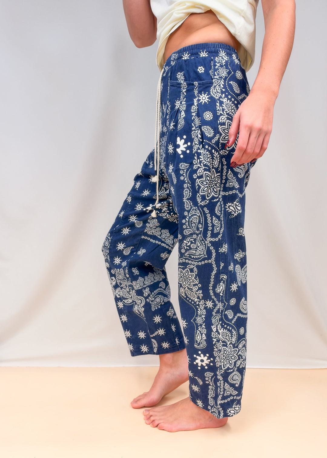 Woman shown from side view waist down wearing blue paisley pull on pants on plain background