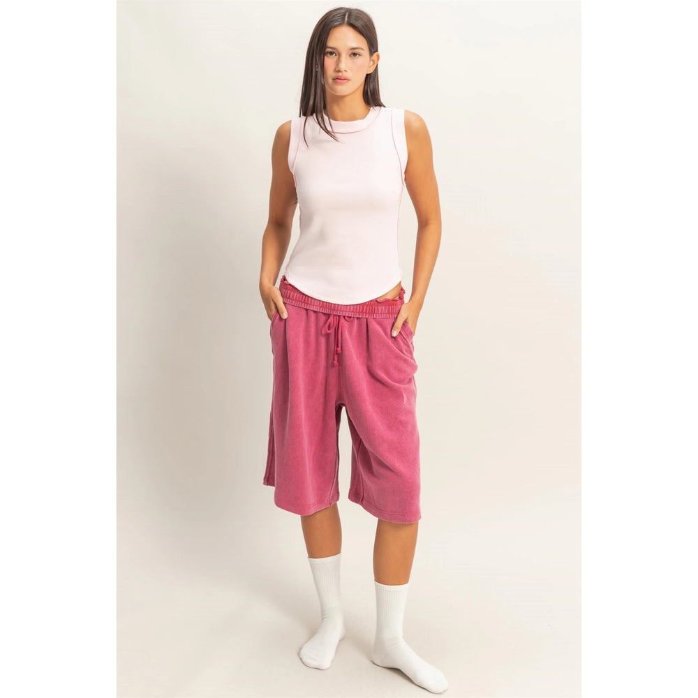 Woman wearing a white sleeveless top and pink capri pants on a plain background