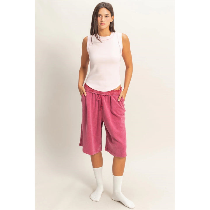 Woman wearing a white sleeveless top and pink capri pants on a plain background