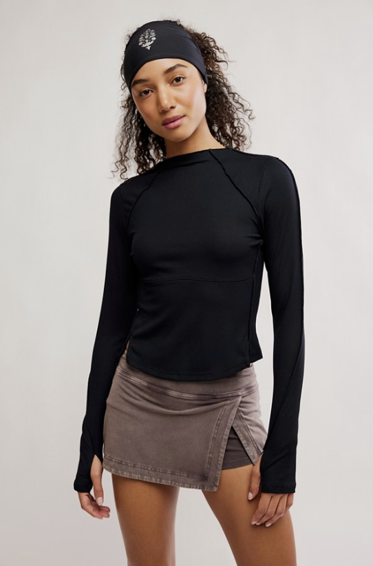 Woman wearing a black long-sleeve top and brown skirt on a plain background