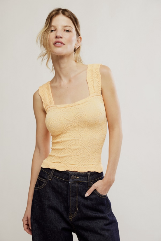 Woman wearing a yellow tank top and dark jeans against a plain background