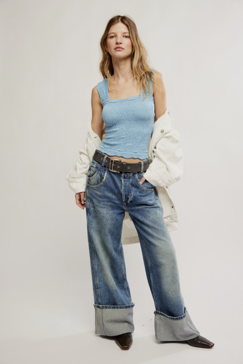 Woman wearing a light blue tank top and jeans with a white jacket on a plain background