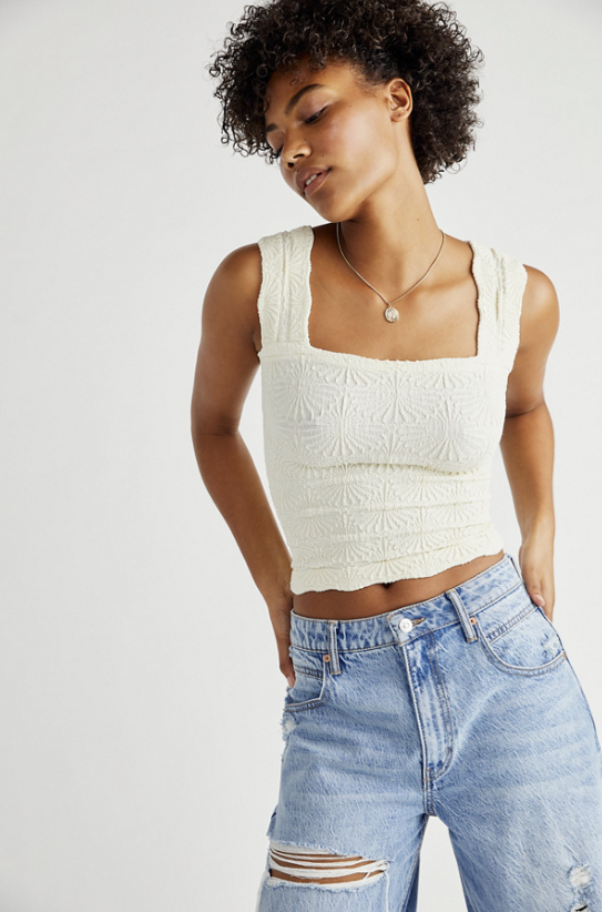 Woman wearing a white sleeveless top and blue jeans against a plain background