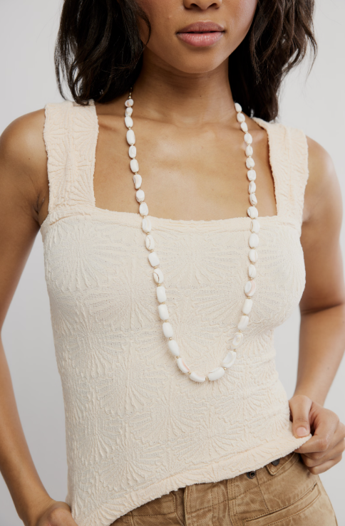 Woman wearing cream tank and shell necklace on plain background