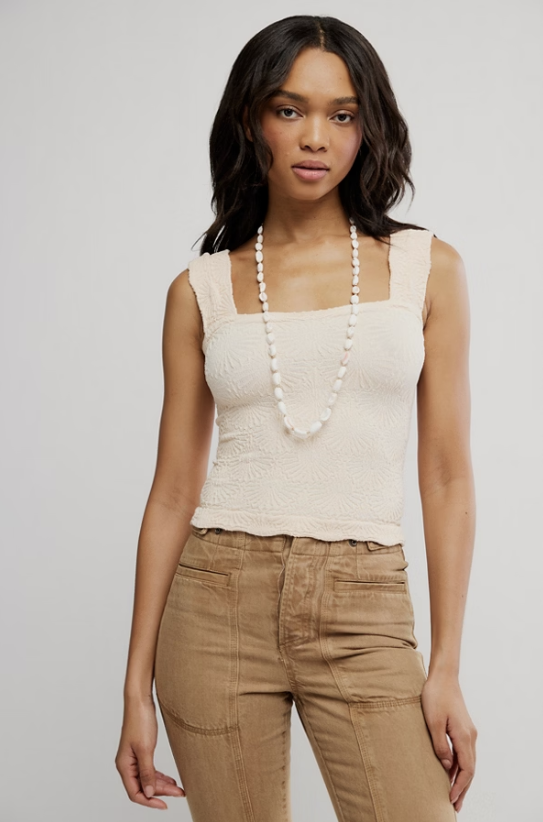 Woman wearing cream tank and khaki pants on plain background