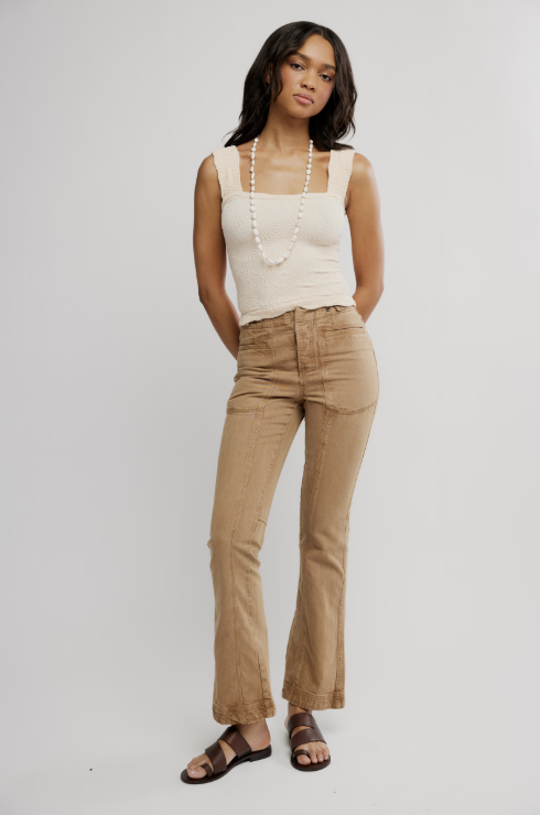 Woman wearing cream tank and khaki pants on plain background