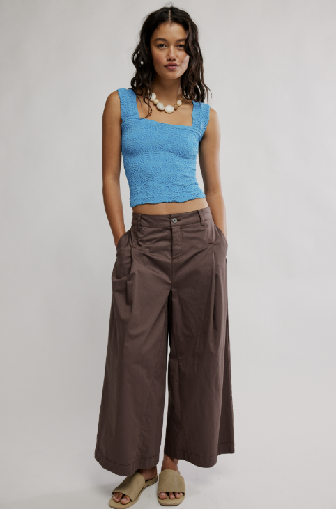 Woman wearing a blue top and brown wide-leg pants on a plain background