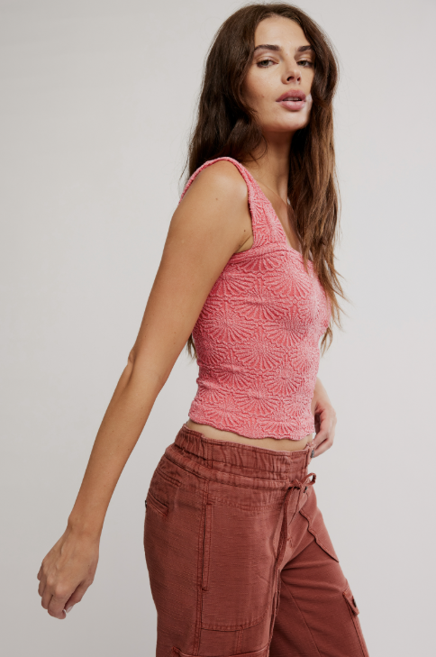 Woman wearing a pink sleeveless top and brown pants on a plain background