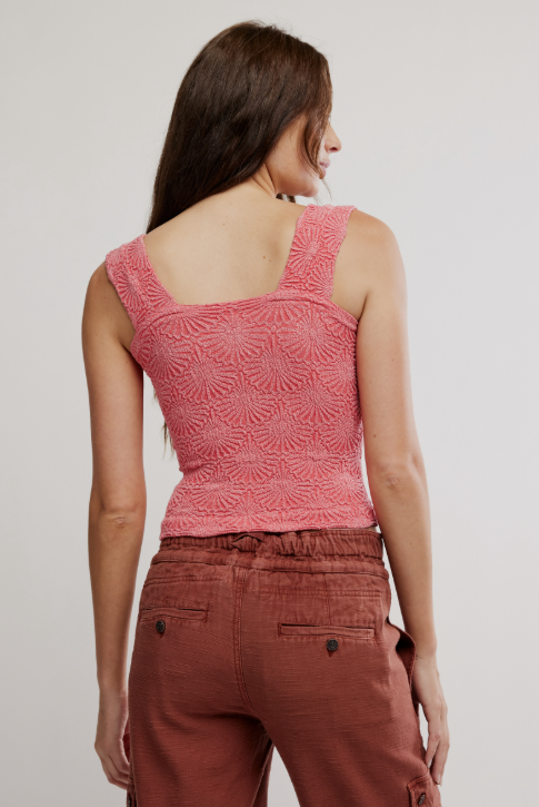 Woman wearing a pink patterned top and brown pants on a plain background