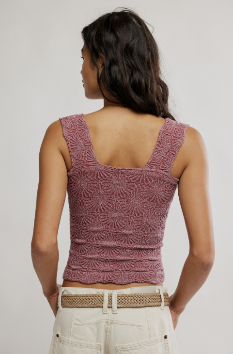 Woman wearing a patterned pink top and beige pants against a plain background