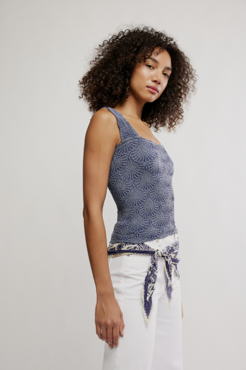 Woman wearing a blue patterned top and white pants against a plain background