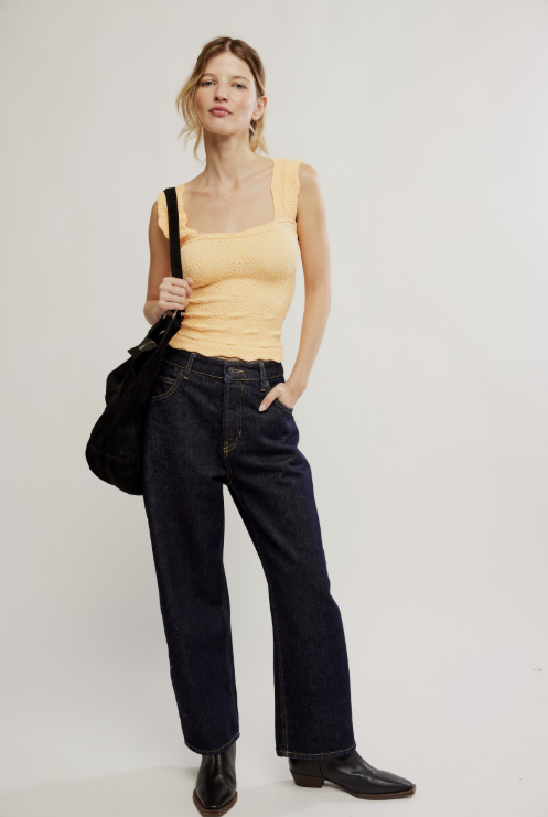 Woman wearing a yellow top and black jeans holding a black bag on a white background