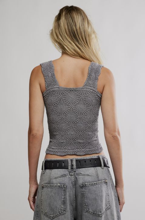 A woman shown from the back wearing a gray textured sleeveless crop top and gray jeans with a black belt, against a light gray studio background.