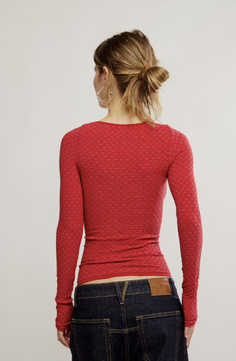 Back of woman wearing long sleeve red textured top with dark denim jeans on white background