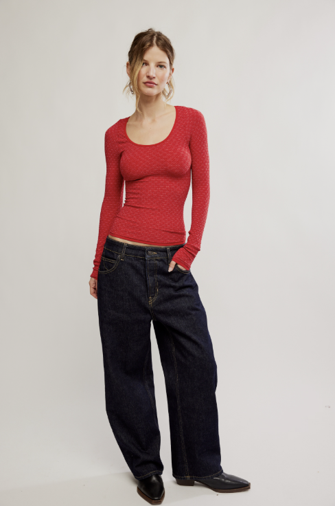 Woman wearing long sleeve red textured top with dark denim jeans on white background