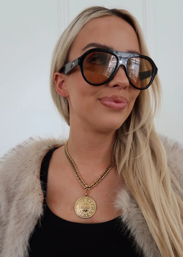 Woman wearing large sunglasses and a fur coat with a plain background