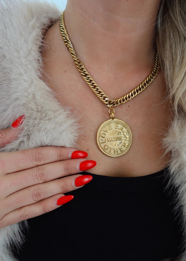 Person wearing a gold chain necklace with a pendant, black top, and fur coat.
