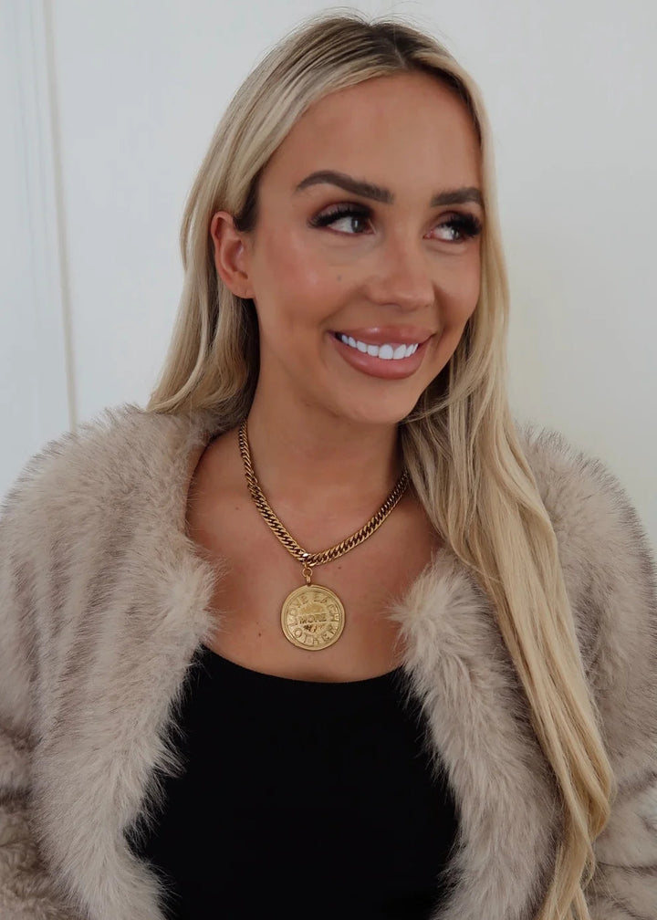 Woman wearing a fur coat, black top, and gold necklace with a coin pendant.