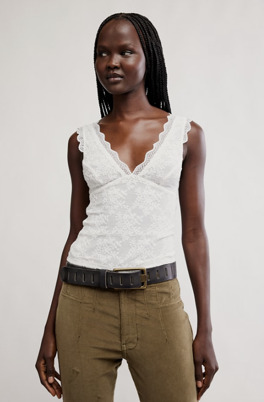 Woman wearing a white lace top and brown pants against a plain background