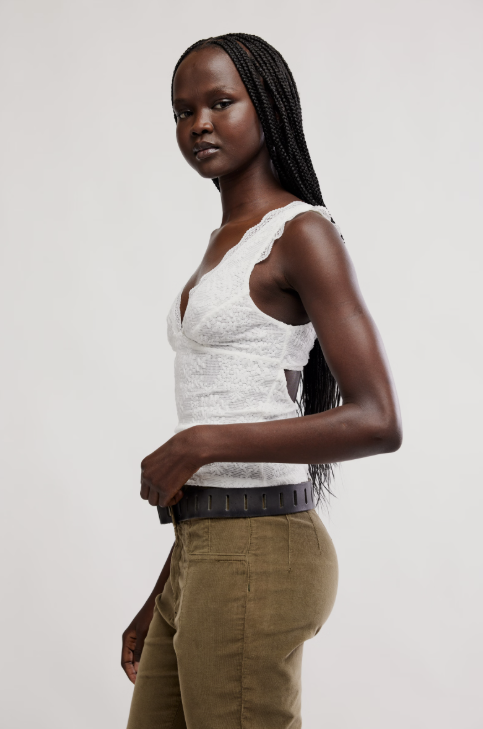 Woman wearing a white lace top and brown pants on a plain background
