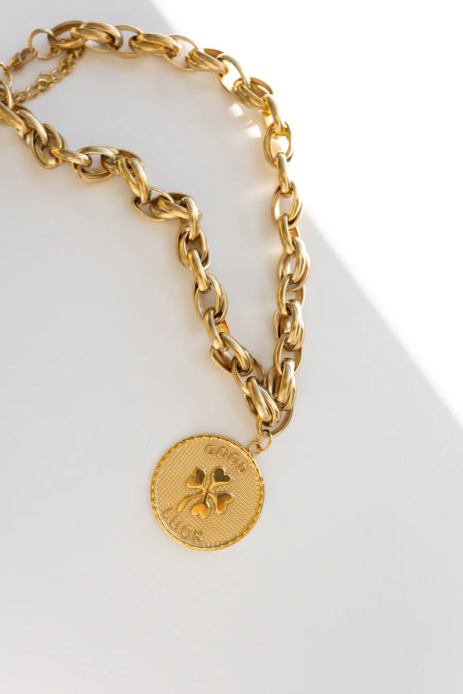 Gold chain necklace with a clover-shaped charm on a white background