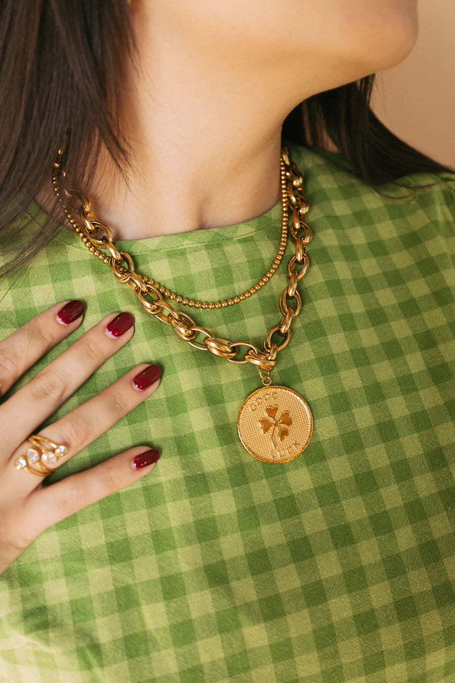 Gold chain necklace with a pendant on a person wearing a green checkered shirt.