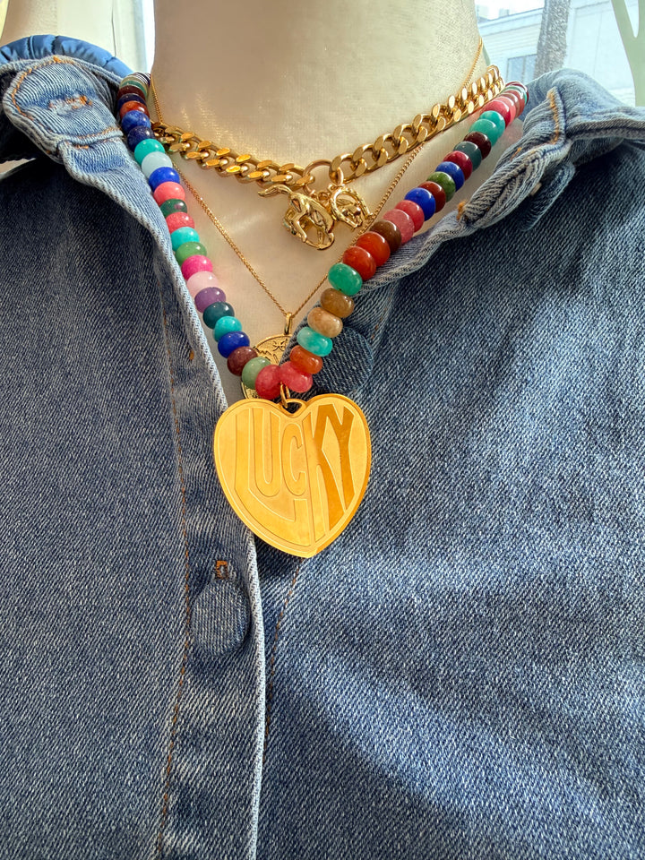 Colorful beaded bracelet with a gold heart charm on a denim surface