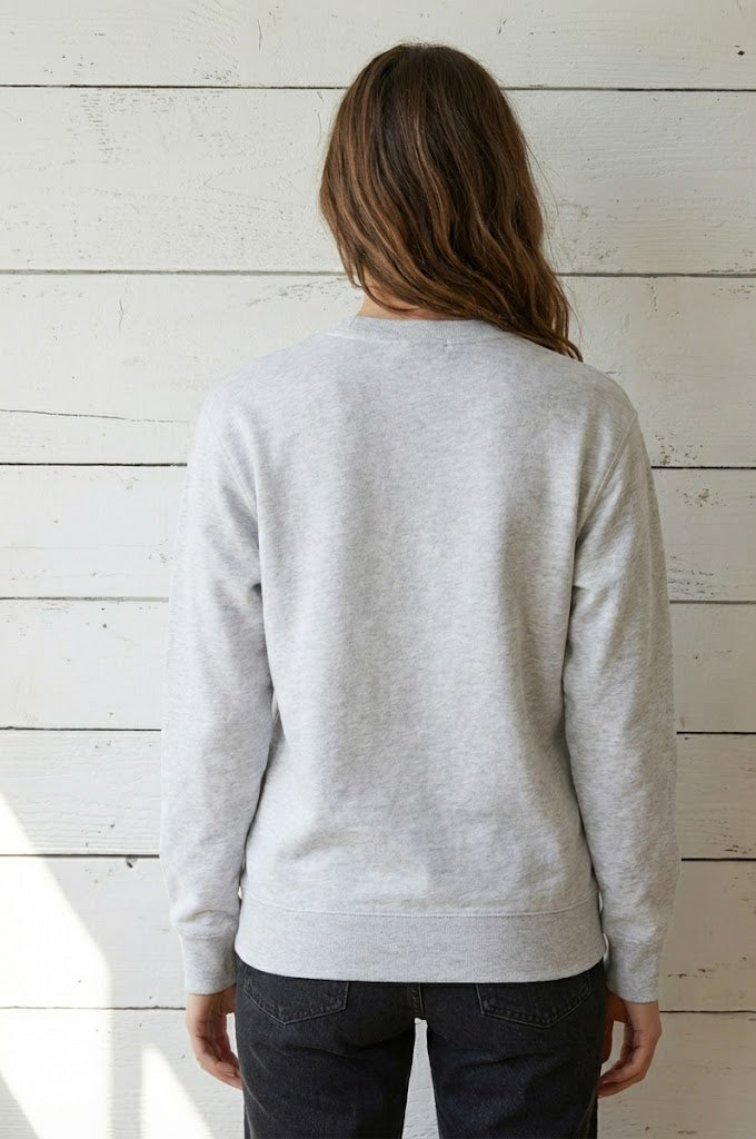 Person wearing a light gray sweater against a white wooden panel background