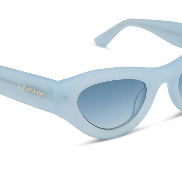 Light blue cat-eye sunglasses with gradient blue lenses and gold script branding on the temple arm, shown on a clean white background.