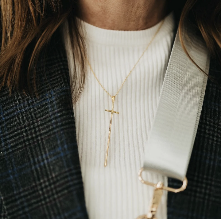 Woman wearing cream shirt showing elongated gold cross necklace