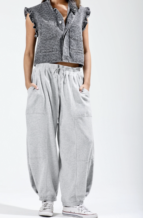 Person wearing a sleeveless denim vest over a crop top with light gray wide-leg pants on a white background